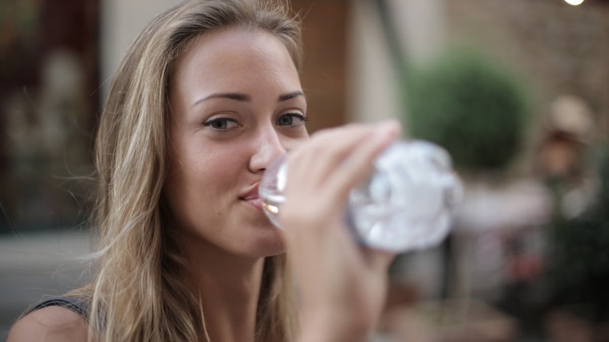 Portrait of a smiling woman drinking bottled water outdoors, enjoying hydration and relaxation.